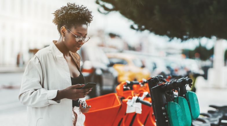 Young woman using her phone to hire an e-scooter